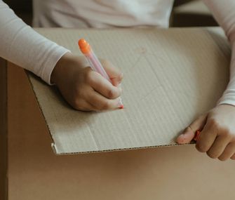 Beschrifte genau, wohin deine Umzugskartons in der neuen Wohnung kommen Person beschriftet Umzugskarton mit Textmarker