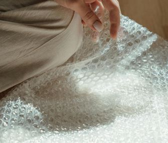 Wählen Sie das passende Material zum Verpacken Ihrer Gegenstände Frau sitzt auf dem Boden mit Luftpolsterfolie