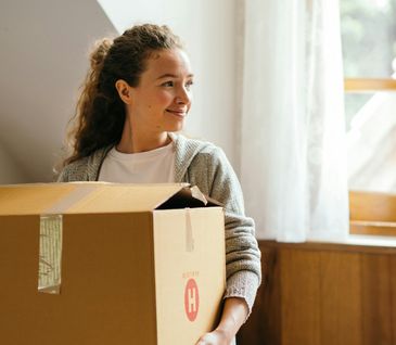 Frau trägt Umzugskarton in heller Wohnung