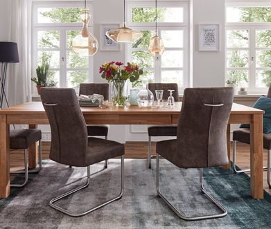 Graue Freischwingerstühle aus Leder mit schwarzen Füßen vor einem Esstisch aus Holz