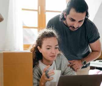 Vorbereitung ist alles: Planen Sie Ihren Umzug bis ins Detail Mann und Frau planen am Laptop zwischen Umzugskartons