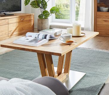 Couchtisch aus Massivholz mit einem modernen Gestell vor einem grauen Hocker