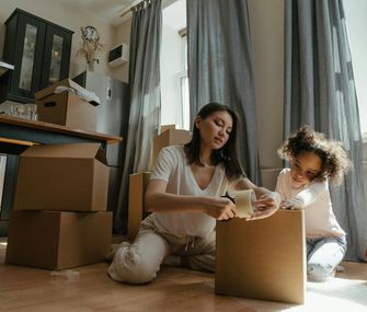 Packe deine Umzugskartons mit System, damit beim Umzug und danach kein Chaos ausbricht Mutter und Tochter packen Umzugskartons in der Küche