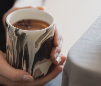 Nahaufnahme schwarz-weißer Glühwein-Tasse mit Frauenhänden