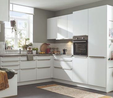 Weiße Küche in L-Form mit silberfarbenen Griffen und grauen Wänden