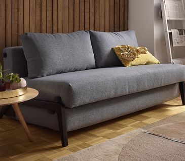 Graues Sofa mit Schlaffunktion und gelben Deko-Kissen neben einem runden Beistelltisch