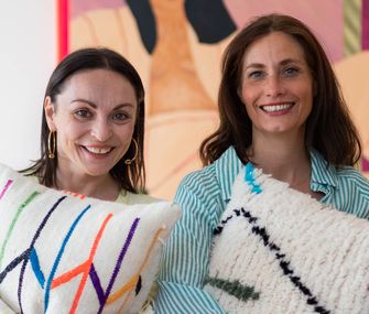 Stylistin Nicole Zweig mit Freundin, bunten Kissen und Bild mit neonpinkem Rahmen im Hintergrund