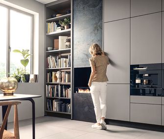 Frau steht vor einer grauen next125 Küche mit Kamin