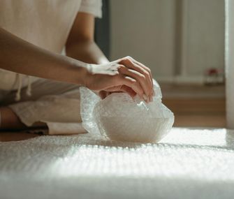 Zeichne Zerbrechliches gut sichtbar auf deinen Umzugskartons aus Person packt zerbrechliche Schale in Luftpolsterfolie ein