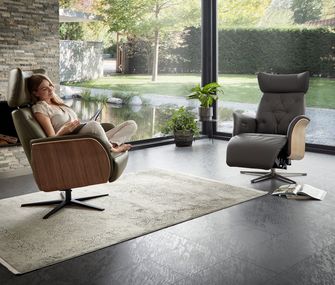 Elegant und modern: Ledersessel mit Holzschale sind richtige Eyecatcher Zwei Ledersessel im hellen Wohnzimmer mit einer lesenden Frau auf dem linken Relaxsessel