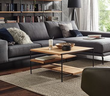 Couchtisch mit Massivholz und schwarzem Metall vor einem dunkelgrauen Sofa und Bücherwand