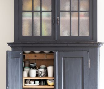 Anthrazitfarbener Küchenschrank mit offener Tür, die Sicht auf Tassen und anderes Geschirr gibt.