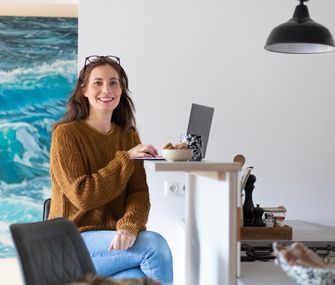 Nicole sitzt mit Laptop auf Barhocker am Küchentresen, um zu arbeiten.
