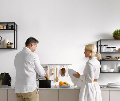 Junges Paar steht in einer modernen Küche ohne Küchenoberschränke mit hellgrauer Küchenzeile.