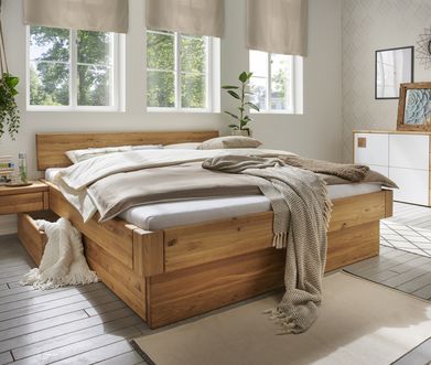 Massivholz-Bett mit grauen und braunen Decken dekoriert neben weißer Kommode