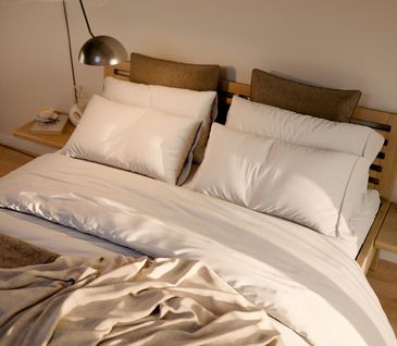 Vogelperspektive auf Bett mit weißen Kopfkissen und beiger Tagesdecke.