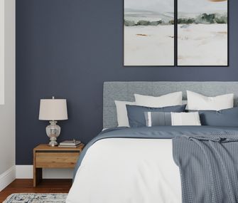 Schlafzimmer mit hellblauem Boxspringbett vor blauer Wand.