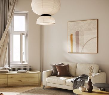 Kleines beiges Stoffsofa vor heller Wand mit Decke, Kissen und Beistelltisch dekoriert.