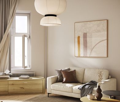 Kleines beiges Stoffsofa vor heller Wand mit Decke, Kissen und Beistelltisch dekoriert.