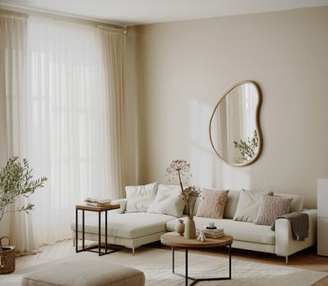 Helles Wohnzimmer im Hygge Stil: Beiges Ecksofa, hellbrauner Hocker, großer Teppich und dekorierte Beistelltische.