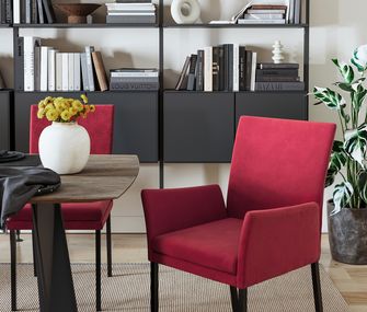 Sattes Rot verändert die Atmosphäre im Zimmer zum Positiven. Probieren Sie es aus. Roter Armlehnstuhl in Esszimmer vor schwarzer Wohnwand neben Esstisch.