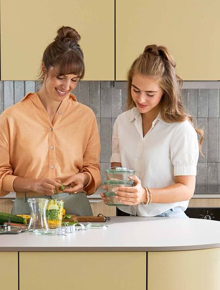 Mutter und Teenager-Tochter stehen gemeinsam in moderner Küche und kochen.