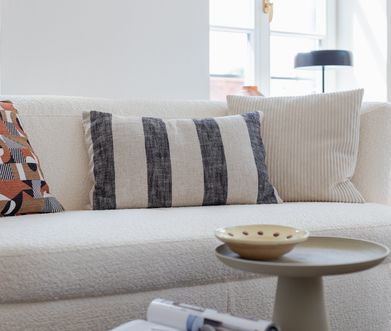 Detailansicht von Sofa in beigem Bouclé, dekoriert mit Kissen und beigem Beistelltisch.