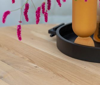 Großaufnahme von Tischplatte aus Eiche Massivholz mit Vase und Blumen.