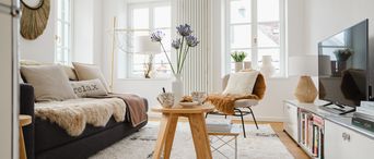 Gemütliches Wohnzimmer mit großem beigem Teppich, Sofa mit Fellen, weißem Sideboard und Couchtisch,