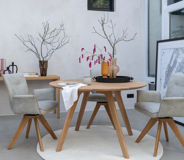 So zieht Nachhaltigkeit bei Ihnen Zuhause ein. Runder Holztisch mit hellgrauen Esszimmerstühlen mit Dekoration.