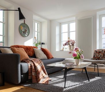 Helles Wohnzimmer mit grauem Sofa, beigem Stuhl und Couchtisch mit Marmorplatte.