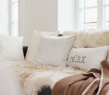 Sofa mit Fellen und Kissen in hellen Tönen dekoriert.