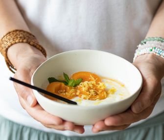 Aprikosenkompott mit Joghurt in einer weißen Schüssel gehalten von einer Frau.