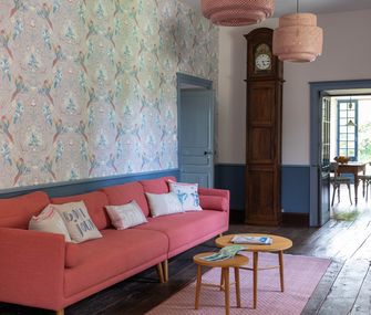 Großes rosanes Sofas im Eingangsbereich vor Wand mit Mustertapete.