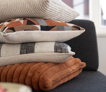 Kissenstapel mit verschiedenen Kissen auf einem grauen Sofa.