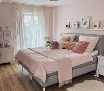 Graues Bett im Landhausstil mit rosa Bettwäsche vor einer hellrosa Wand.