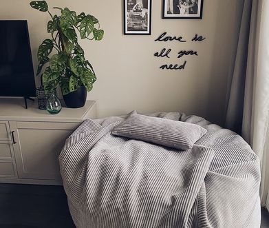 Grauer Sitzsack vor einer Wand mit Bild und Schriftzug.