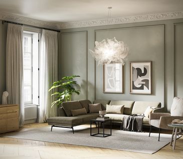 Das sanft-grüne Ecksofa Estrela bringt natürliche Harmonie in Ihr Wohnzimmer - jetzt bei Homepoet entdecken Salbeigrünes Sofa vor passender Wand auf hellem Teppich mit beigem Sessel und Couchtisch