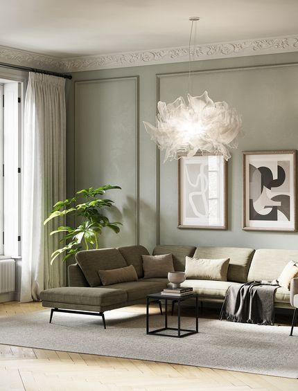 Salbeigrünes Sofa vor passender Wand auf hellem Teppich mit beigem Sessel und Couchtisch