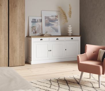 Schlafzimmer im Hygge Stil mit rosa Sessel, weißem Sideboard und Holzschrank.