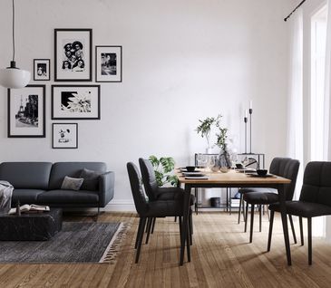 Wohn und Essbereich mit schwarzem 2-Sitzersofa und großem Esstisch mit sechs schwarzen Lederstühlen. Großes helles Fenster und mit Bildern dekorierte Wand.