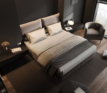 Graues Bett mit hellgrauen Kissen und Tagesdecke vor anthrazitfarbener Wand. Sessel steht neben Bett.