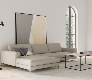 Ein beiges Ecksofa und ein Couchtisch mit beiger Tischplatte und schwarzem Metallgestell vor einer weißen Wand mit einem großen Bild.