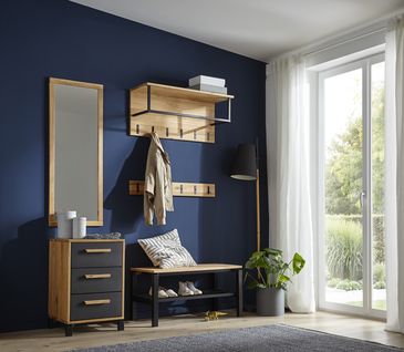 Garderoben-Set aus Sitzbank, Hängeelement, Kleiderhaken, Spiegel, und Kommode vor dunkelblauer Wand neben großem Fenster.