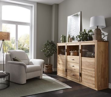 Beiger Stoffsessel neben Sideboard aus Massivholz in Wohnzimmer.