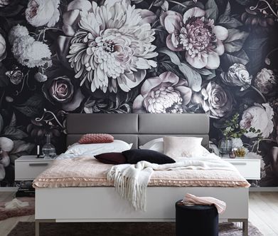 Doppelbett mit grauer Rückenlehne und rosa Decke vor Wand mit Blumentapete