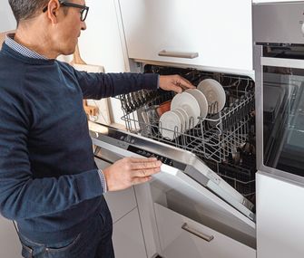 Ein Mann räumt eine hochgebauter Spülmaschine ein