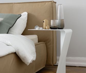 Detailbild von einem modernen Bett in cappuccinofarbenem Leder mit weißem Beistelltisch.