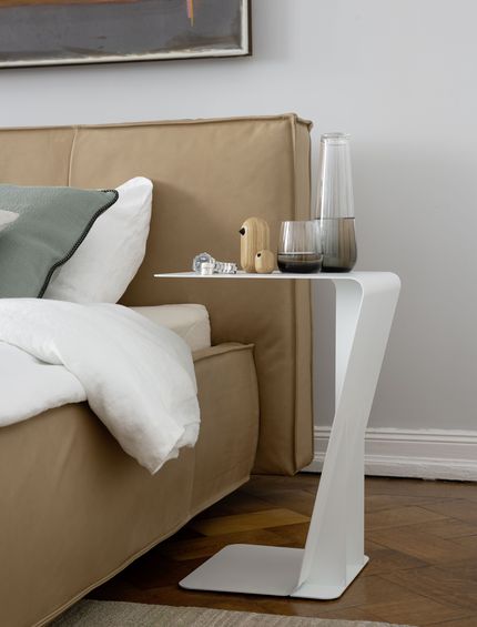 Detailbild von einem modernen Bett in cappuccinofarbenem Leder mit weißem Beistelltisch.