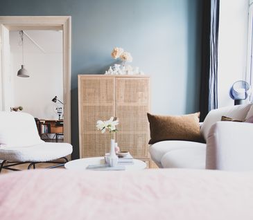 Helles Wohnzimmer mit weißer Couch, weißem Teddy-Schwingsessel und Kommode